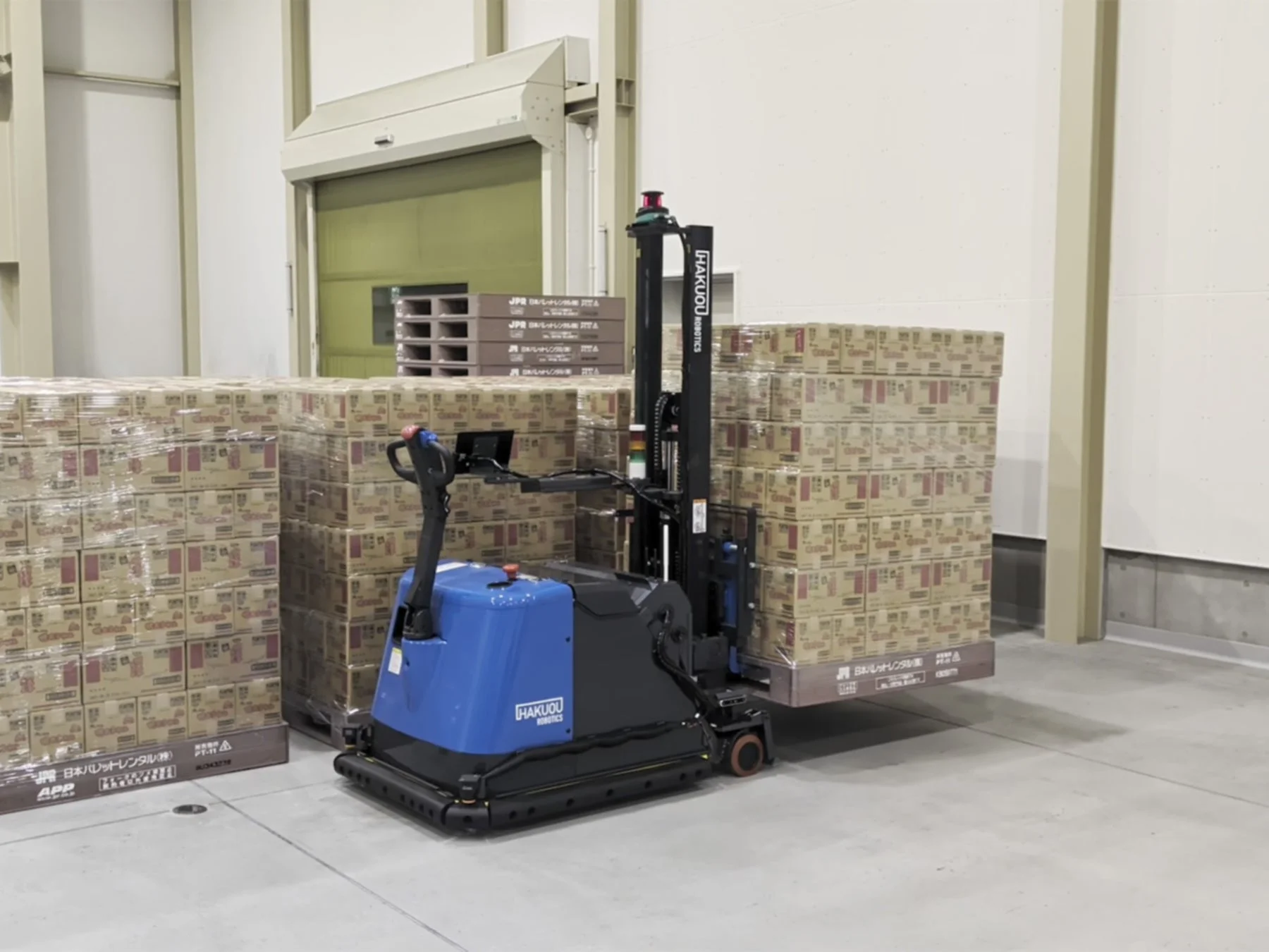 倉庫内でHAKUOU ROBOTICS製の自動フォークリフトがパレットに積まれた段ボール箱を搬送している様子です。効率的な物流作業を示すシーンです。