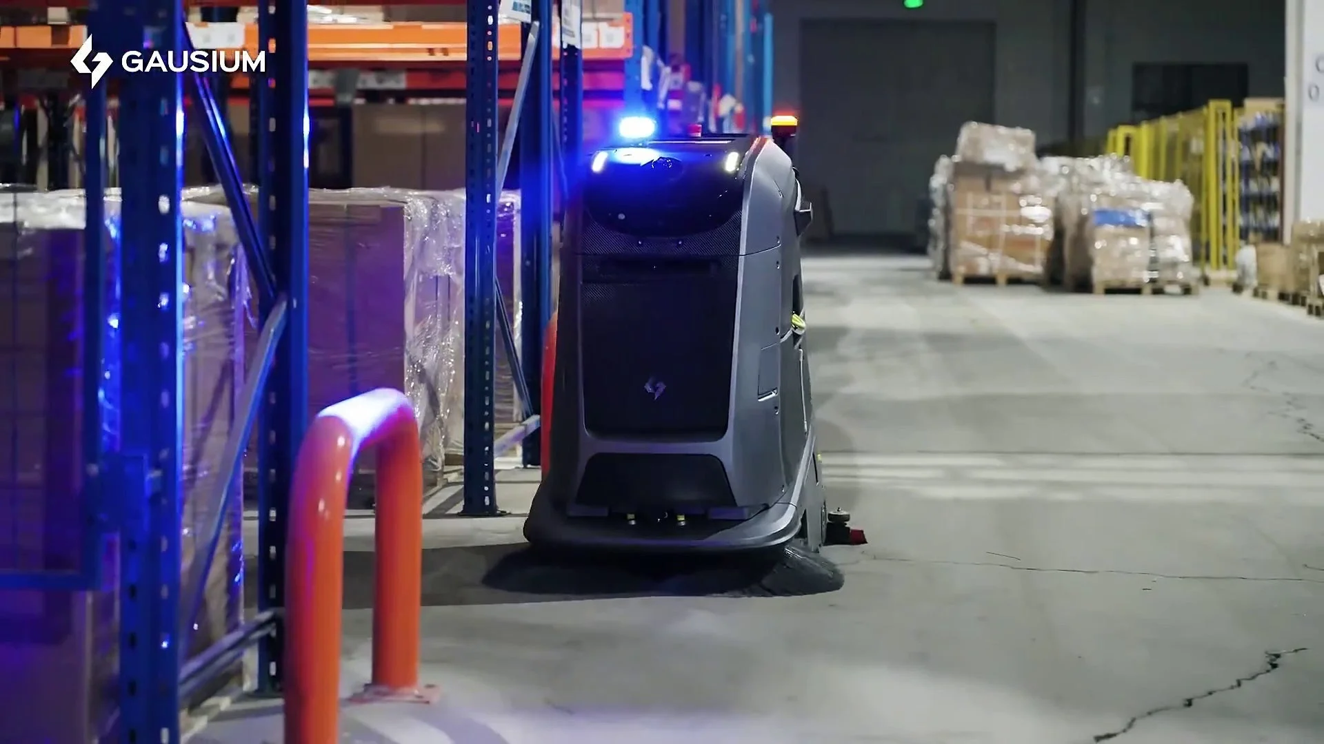 倉庫内で自動床洗浄ロボット「GAUSIUM」が青い光を放ちながら床を清掃している様子。高層棚には多くの荷物が積まれ、効率的な物流環境が伺えます。