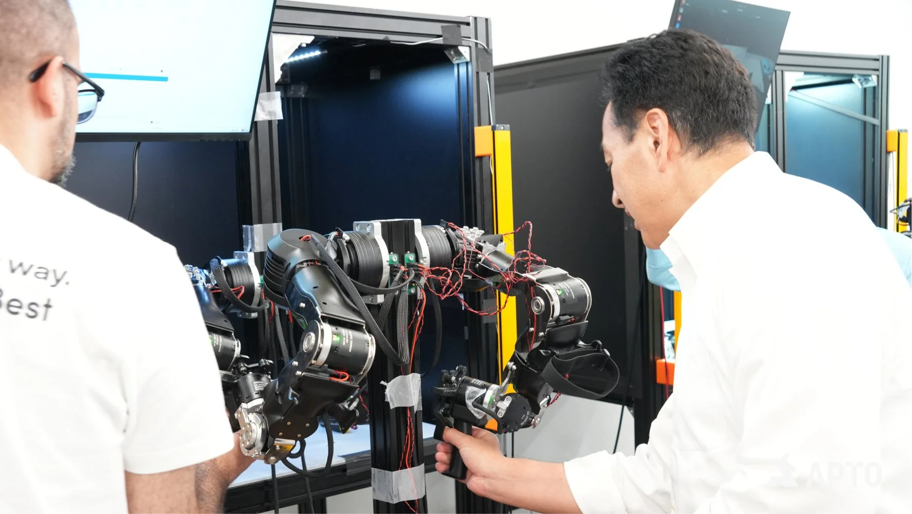 2人の男性が、複雑な配線を持つロボットアームシステムを操作・調整している様子