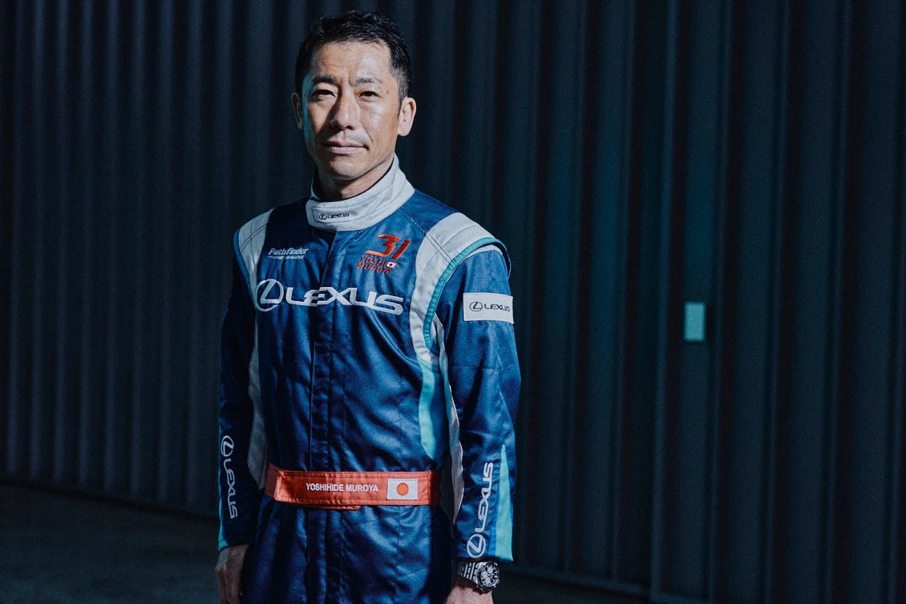 青と白のレーシングスーツを着用した日本人男性のポートレート。スーツには「LEXUS」や「YOSHIHIDE MUROYA」の文字があり、真剣な表情でカメラを見つめている。プロのレーサーの雰囲気が伝わる一枚です。