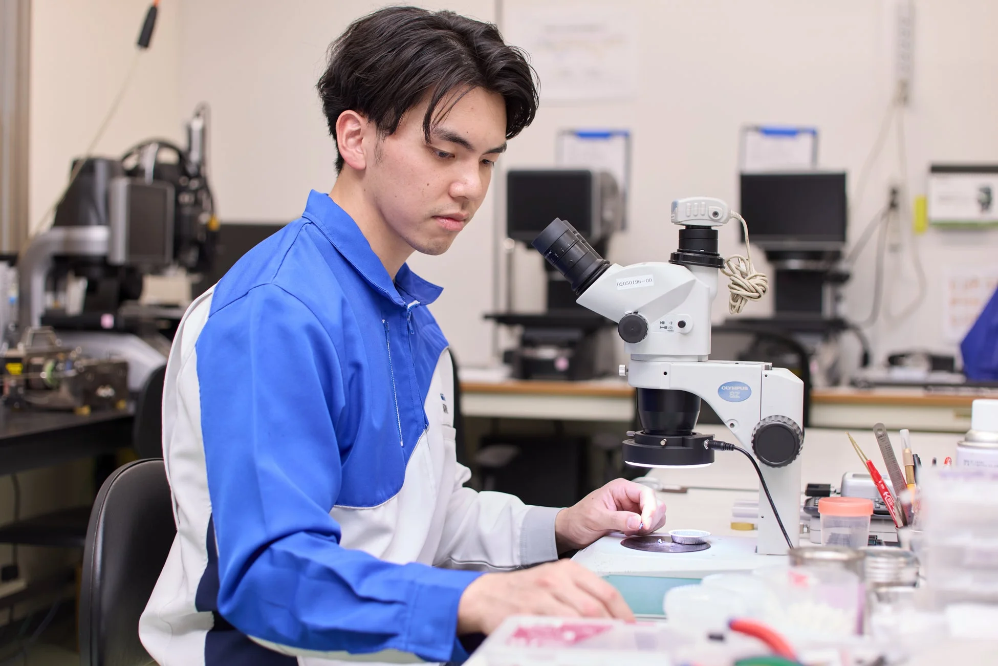 研究室で顕微鏡を使い、小さな部品を検査する男性