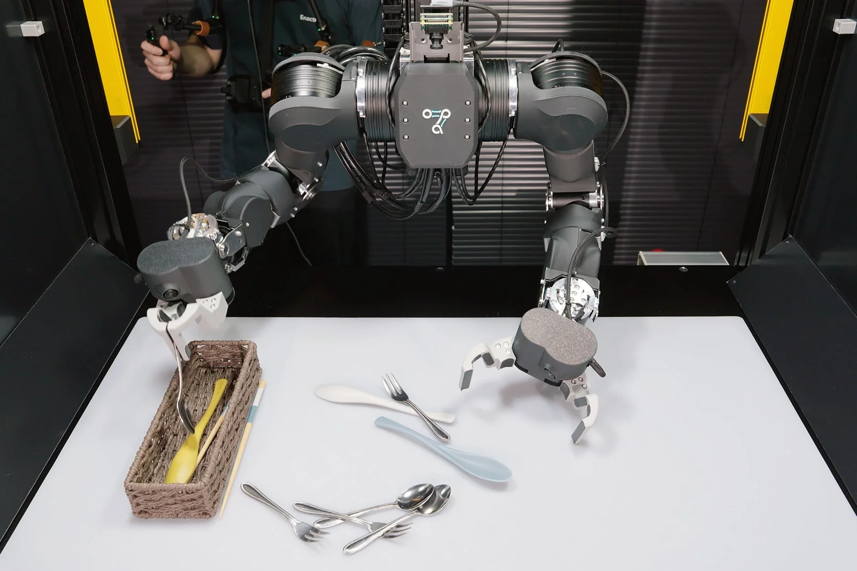 人間がコントローラーでロボットアームを操作し食器を整理する様子