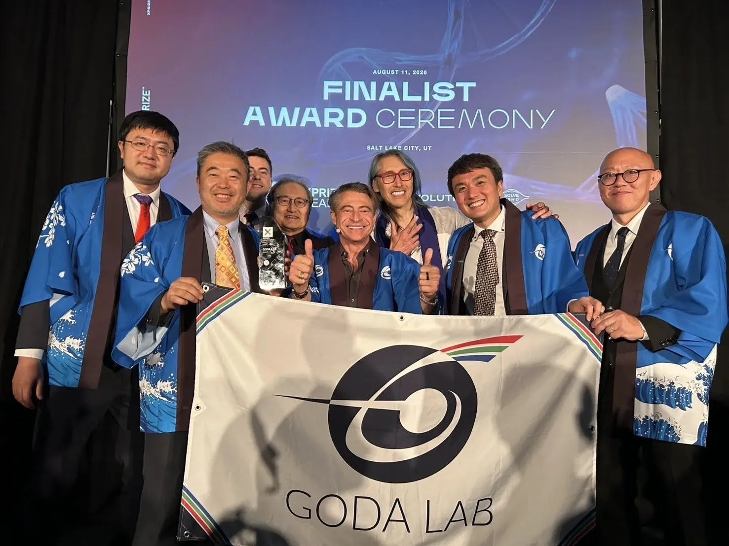 GODA LABのメンバーがトロフィーとバナーを掲げた集合写真