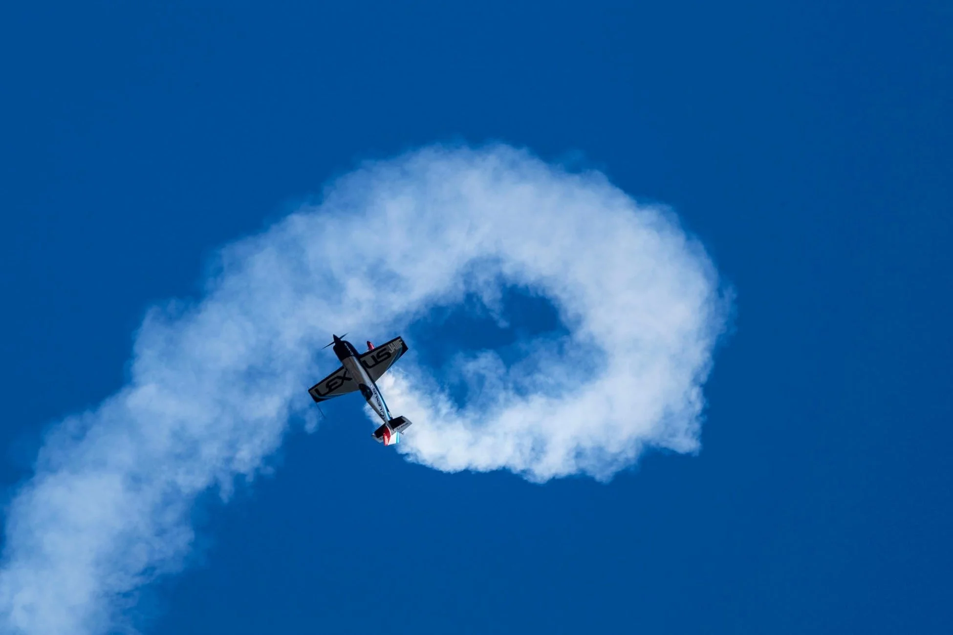 青空を背景に、アクロバット飛行中の飛行機が白いスモークでループを描いている瞬間を捉えたダイナミックな画像です。
